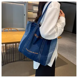 Detailed view of large denim tote bag with blue patchwork and orange embroidery