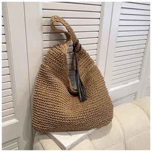 Detail of hand-woven straw hobo bag with wide shoulder strap and brown leather tassel