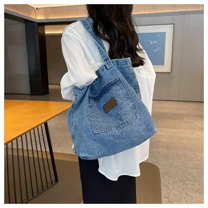 Detail of blue denim tote bag showing wide shoulder strap and leather patch on back view