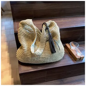 Detail of a beige woven straw tote bag with brown leather handles and a long tassel