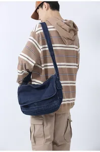 Detail of a large dark blue denim messenger bag worn by a model in casual striped sweater