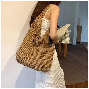 Detail view of large straw hobo bag with wide shoulder strap and black tassel charm