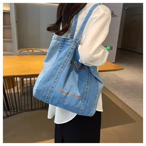Detail shot of light blue denim tote bag with orange embroidery and sturdy shoulder strap
