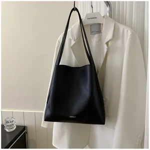 Detailed view of black matte leather tote bag hanging on a white blazer outfit