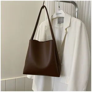 Detail view of large dark brown leather tote bag against a white suit background