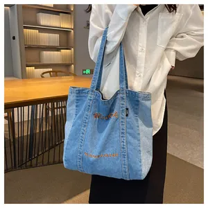 Detail of blue denim tote bag with brown letter embroidery and durable fabric texture