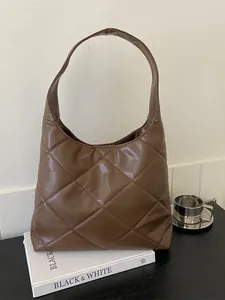 Brown quilted rhombic tote bag made of PU leather with wide shoulder strap on books