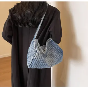 Close-up of quilted blue denim shoulder bag with vertical stitching and metal zipper detail