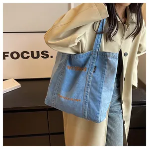 Close-up of light blue denim tote bag featuring orange WISDOA embroidery and wide strap