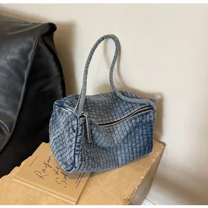 Close-up of quilted denim shoulder bag showing blue fabric texture and metal zipper detail