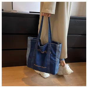 Detail of denim tote bag with blue patchwork and orange WISDOR embroidery on the front