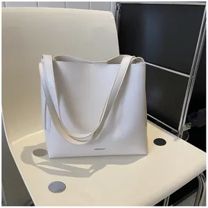 Side view of cream-white large capacity tote bag with long strap on minimalist chair