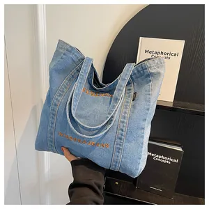 Close-up of light blue denim tote bag featuring orange embroidered brand lettering