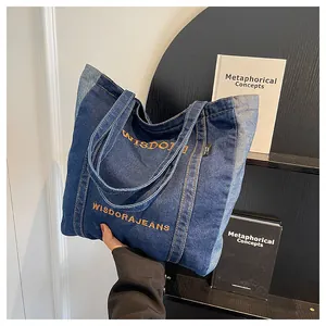Detail of blue denim tote bag with contrast stitching and yellow embroidered text