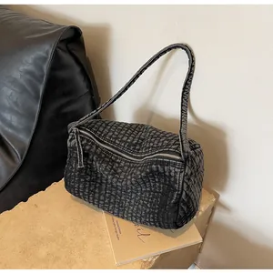 Detail of washed denim shoulder bag with quilted texture and metal zipper on stone surface