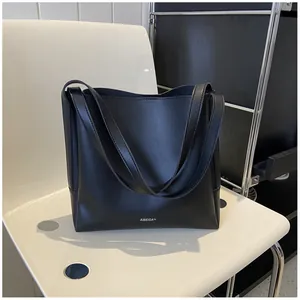 Detail of matte black leather tote bag with silver brand logo on white chair