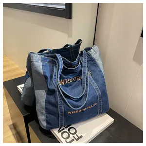 Detail of color-block denim tote bag showing blue patchwork and brown embroidery