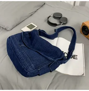 Detail of a large dark blue denim messenger bag with flap closure on a grey surface