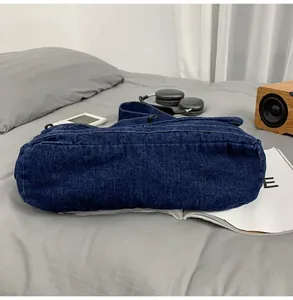Detail of blue denim messenger bag with white stitching on bed with lifestyle props