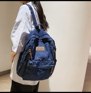 Detail showing the denim texture and brown leather pullers of the blue backpack