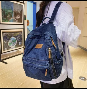 Detail of dark blue denim backpack with side zipper pockets and leather pull tabs