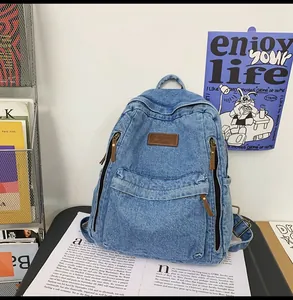 Close-up of vintage blue denim backpack featuring leather logo and multiple zippers