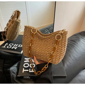 Detalle de bolso de paja tejido con cadena de acrílico ámbar sobre sofá de cuero