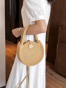 Sac à main rond en paille tressée avec bouton en bois sur robe blanche