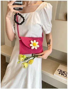 Gros plan d'un sac bandoulière en paille tressée rose avec détail marguerite