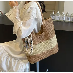 Detail of bohemian tricolor straw tote bag featuring decorative evil eye tassel and fringe