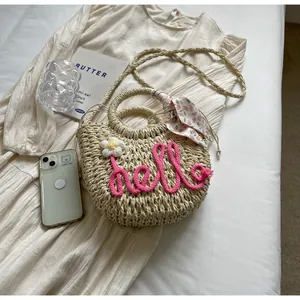 Close-up of woven straw bag with hello embroidery, floral scarf handle, and long shoulder strap