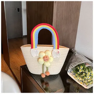 Détail du sac tressé avec anses arc-en-ciel et un grand charme en peluche de tournesol