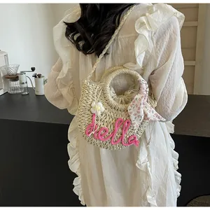 Detail of straw woven bag with pink hello embroidery and floral scarf on a white dress