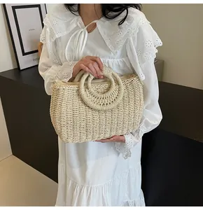 Dettaglio della borsa in paglia beige con ampi manici circolari tenuta da una modella