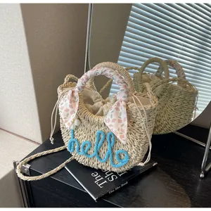 Close-up of straw handbag with hello embroidery, floral scarf handle and flower charm