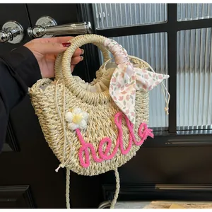 Detail of woven straw bag with pink hello lettering, floral accent, and scarf handle