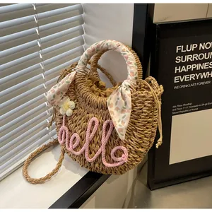 Detailed view of straw bag with hello embroidery and decorative floral scarf on handle