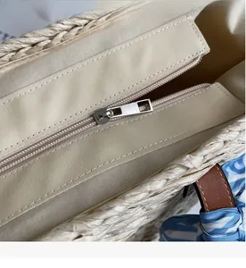 Detail of straw bag with smooth silver zipper closure and blue striped scarf handle