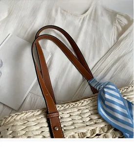 Close-up of straw tote bag with brown leather handles and a blue striped silk scarf detail