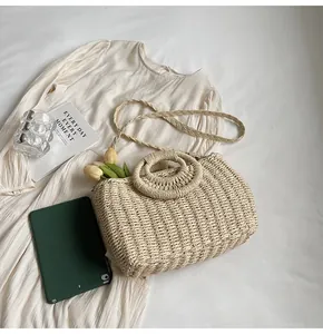 Dettaglio di una borsa in paglia intrecciata con manici rotondi e tracolla sottile