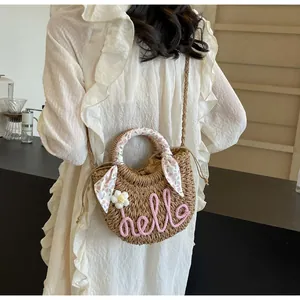 Detail of straw crossbody bag with pink 'hello' lettering and floral scarf handle decor