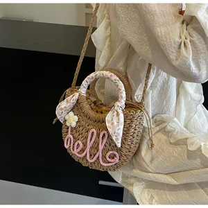 Detail of straw woven bag featuring pink hello embroidery and floral scarf handle