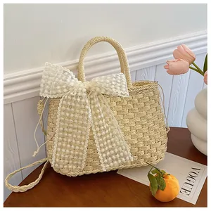 Detalle de bolso de paja trenzada con gran lazo de encaje blanco y asas redondas