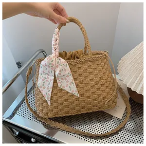 Detalle del bolso de paja tejido con pañuelo floral rosa y cierre de cordón
