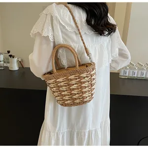 Detail of a brown woven straw handbag with a curved handle and matching shoulder strap
