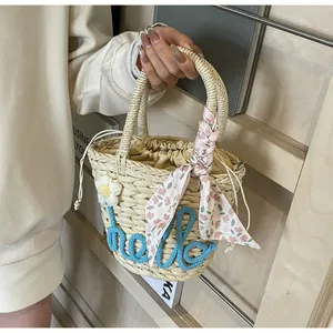 Detail of woven straw bag with blue hello embroidery and floral scarf on handle