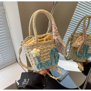 Detail of woven straw bucket bag with blue hello embroidery and floral silk scarf