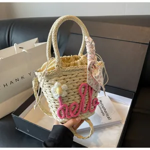 Detail of woven straw handbag with pink hello embroidery and floral scarf decoration