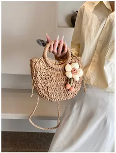 Dettaglio della borsa in paglia intrecciata con fiori in tessuto bianco e pendente rosa