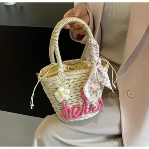 Detail of straw woven handbag featuring hello embroidery and a pink floral scarf handle